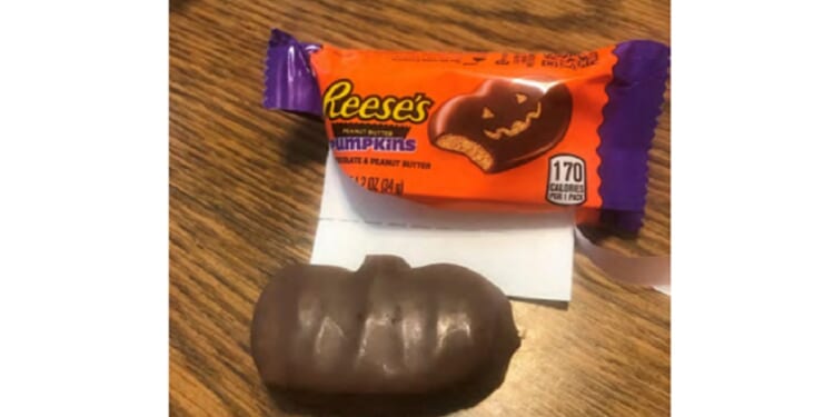 A picture of a Reese's candy wrapper with an illustration that shows a chocolate pumpkin with a carved face, but the candy also shown in the photo has no carving at all.