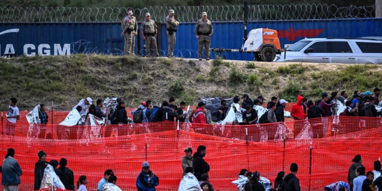 Customs and Border Protection agents stand guard as immigrants wait to be processed after illegally crossing the border from Mexico at Eagle Pass, Texas, on Dec. 22.