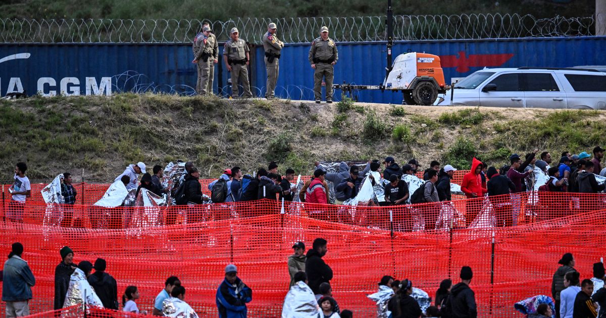 Customs and Border Protection agents stand guard as immigrants wait to be processed after illegally crossing the border from Mexico at Eagle Pass, Texas, on Dec. 22.