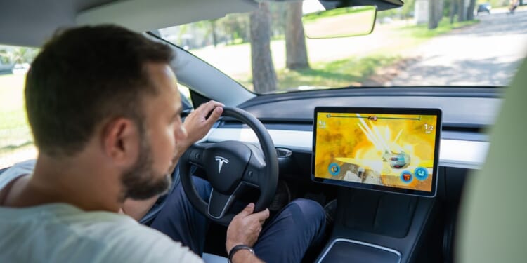 A man looks at the dashboard while driving a Tesla in this stock image.