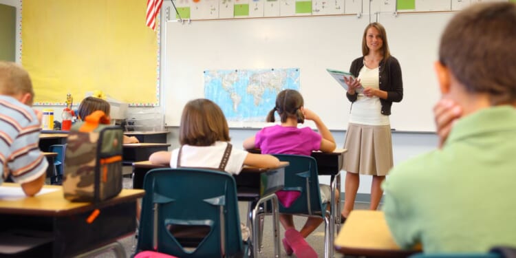 A teacher stands in front of a class in the above stock image.