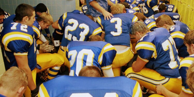 This stock image shows a high school football team praying before a game.