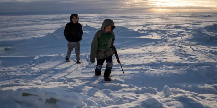 Alaska residents George Chakuchin, left, and Mick Chakuchin walk in the snow with a rifle near Toksook Bay, Alaska, Jan. 18, 2020.