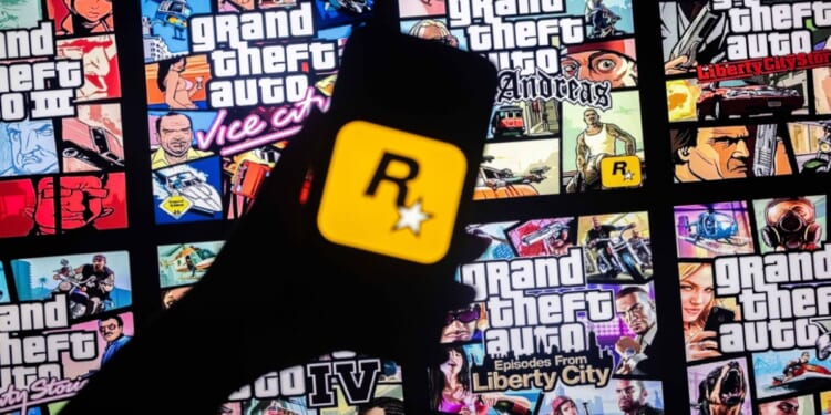 The logo of Rockstar Games on a smart phone in front of the covers of various Grand Theft Auto games.