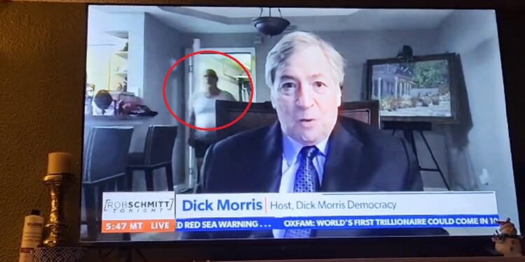 Political pundit Dick Morris speaks during a Newsmax interview when a man clad only in underwear enters the room behind him.