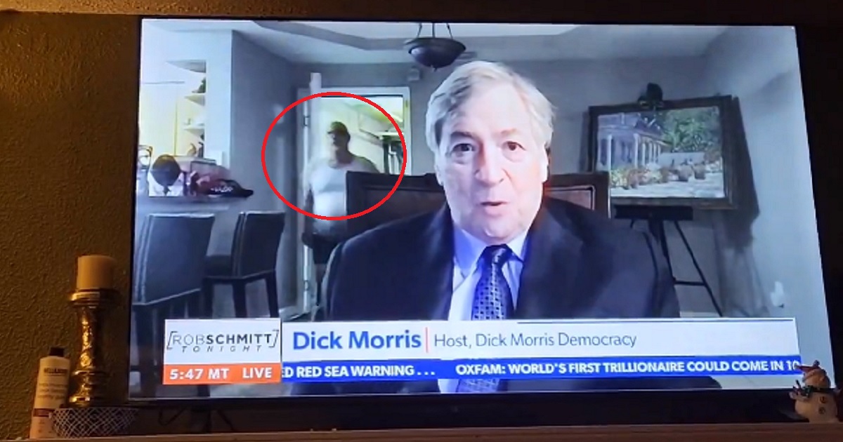 Political pundit Dick Morris speaks during a Newsmax interview when a man clad only in underwear enters the room behind him.