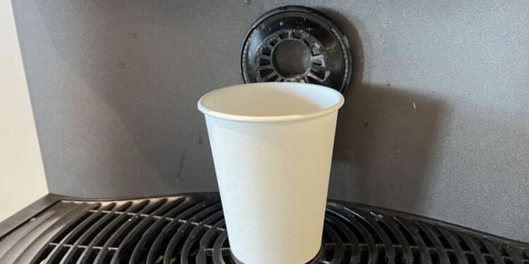 A paper cup is shown on a commercial coffee machine.