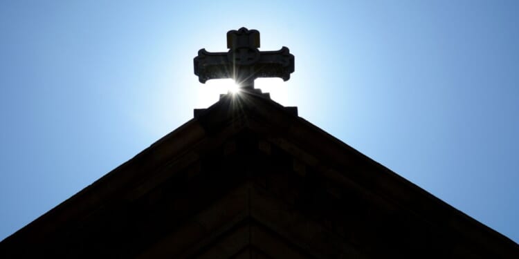 The morning sun rises behind a stone cross atop The Cathedral Basilica of St. Francis of Assisi, commonly known as Saint Francis Cathedral, in Santa Fe, New Mexico.