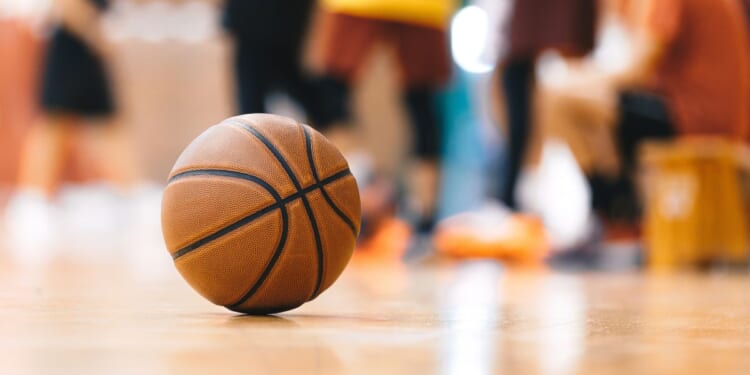 A basketball is scene on a hardwood floor with a youth team in the background.