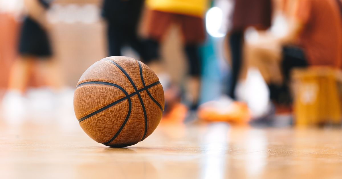 A basketball is scene on a hardwood floor with a youth team in the background.