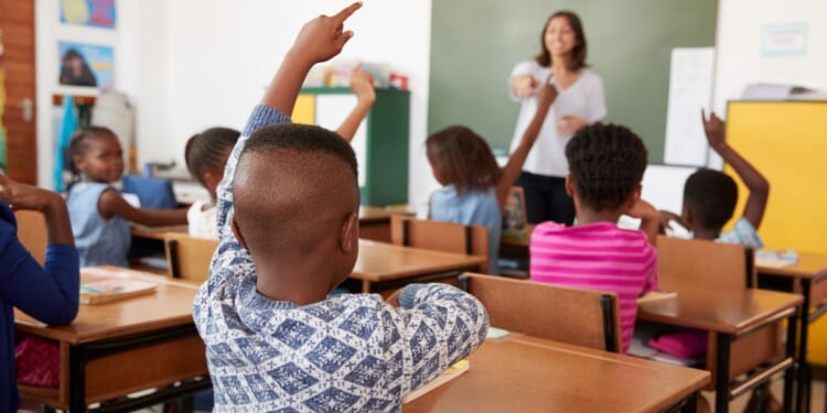 A stock photo shows children raising their hands in a classroom.