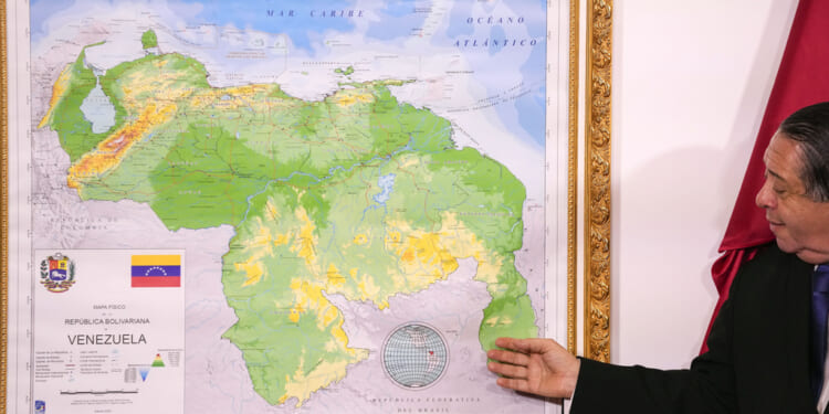 Chairman of the Special Commission for the Defense of Guyana, Essequibo Hermann Escarra, stands next to Venezuela's new map that includes the Essequibo territory, a swath of land that is administered and controlled by Guyana but claimed by Venezuela.