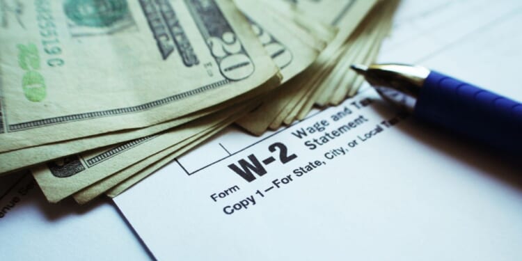 This stock image shows a stack of cash next to a W-2 form.