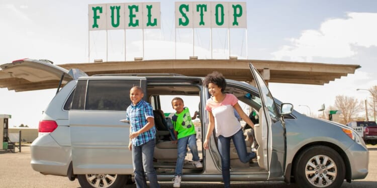 This stock image shows a family getting out of their gas-powered minivan at a gas station.