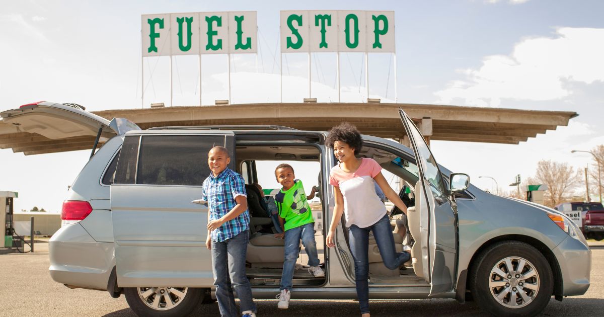 This stock image shows a family getting out of their gas-powered minivan at a gas station.