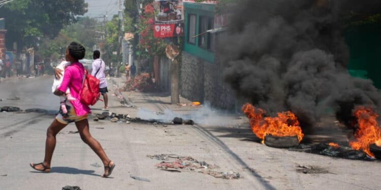 A woman carrying a child runs from the area after gunshots were heard in Port-au-Prince, Haiti, on March 20.