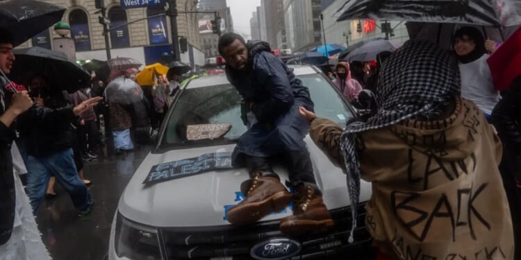 A pro-Hamas demonstrator sits on the hood of a New York City police vehicle that's surrounded by Hamas sympathizers Saturday in Manhattan.