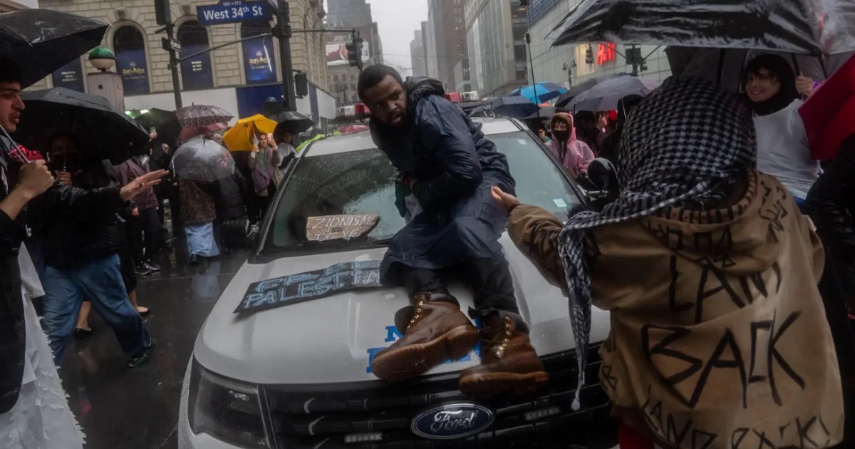 A pro-Hamas demonstrator sits on the hood of a New York City police vehicle that's surrounded by Hamas sympathizers Saturday in Manhattan.