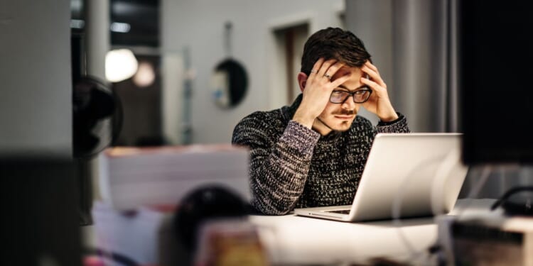 A businessman holding his head in his hands while looking at a computer screen.