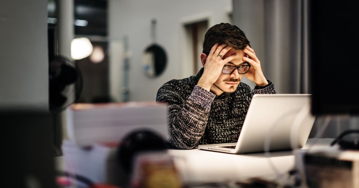 A businessman holding his head in his hands while looking at a computer screen.