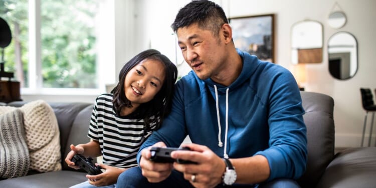 This stock image shows a father and daughter playing video games.