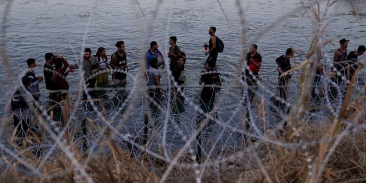 Illegal immigrants waiting in the Rio Grande to climb over concertina wire into the U.S.