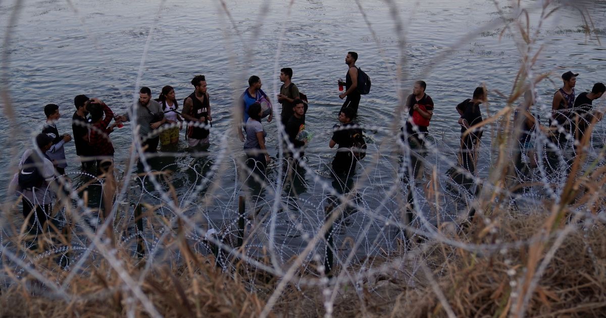 Illegal immigrants waiting in the Rio Grande to climb over concertina wire into the U.S.