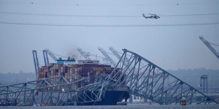 a helicopter flying over the container ship Dali as it rests against wreckage of the Francis Scott Key Bridge