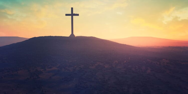 A cross is shown on a hill in the desert.