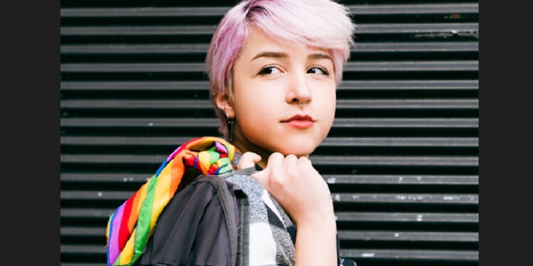 A young person of indeterminate gender with pink hair looking pensive.