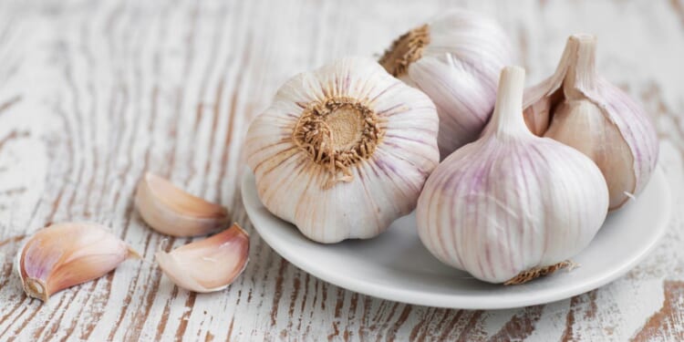 Four garlic bulbs are sitting on a white plate with 3 cloves of garlic next to them.