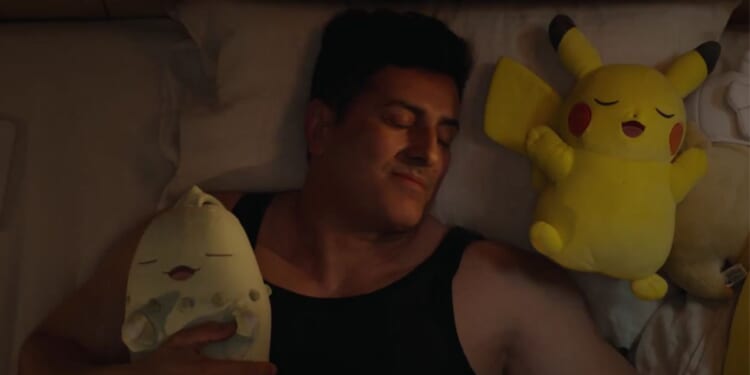 A man in a tank top cuddles up to two Pokémon plushies.