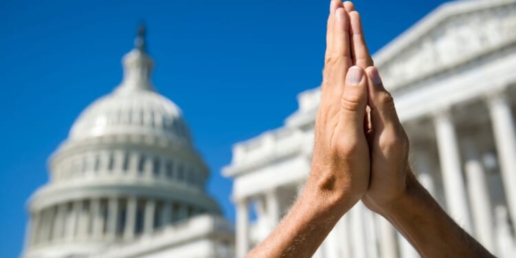 This picture shows hands held together in prayer in front of U.S. Capitol Building in Washington, D.C.