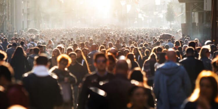 This pictures shows a blurred crowd of people walking down a street during the day.