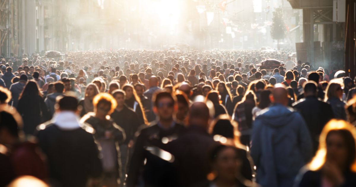 This pictures shows a blurred crowd of people walking down a street during the day.