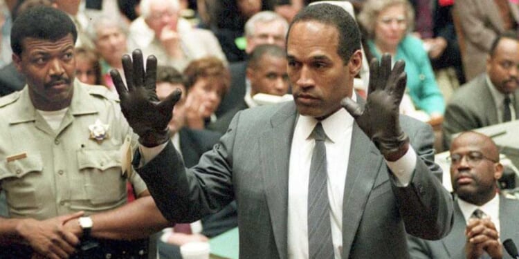 O.J. Simpson shows the jury a new pair of Aris extra-large gloves, similar to the gloves found at the Bundy and Rockingham crime scene 21 June 1995, during his double murder trial in Los Angeles,CA. Deputy Sheriff Roland Jex(L) and Prosecutor Christopher Darden (R) look on.