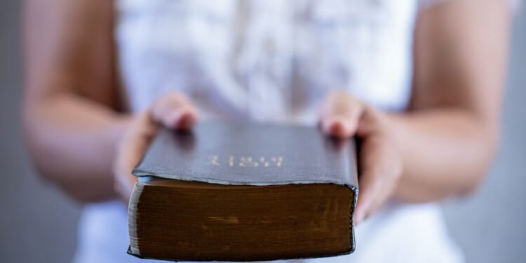 In this photo, a woman is holding out a Bible, offering it to anyone who would like to read it.