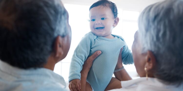 A stock photo shows a couple holding their grandchild.