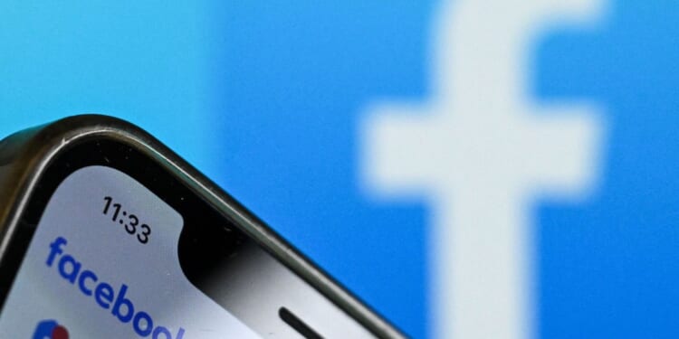 The logo of Facebook on the screen of a smartphone with another Facebook logo out of focus in the background.