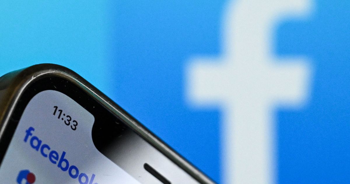 The logo of Facebook on the screen of a smartphone with another Facebook logo out of focus in the background.