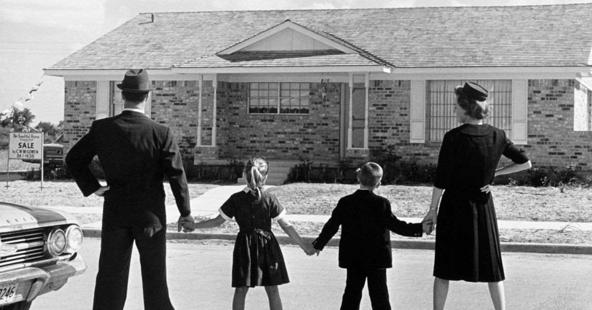 This Getty stock image shows a family in 1950 standing outside of a house for sale.