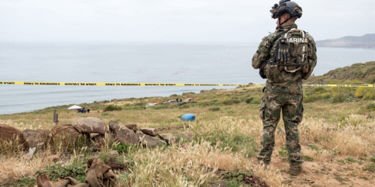 A Mexican marine stands guard near La Bocana Beach in Baja California on Friday as investigators work where the bodies believed to be a missing American and two Australian brothers were found.