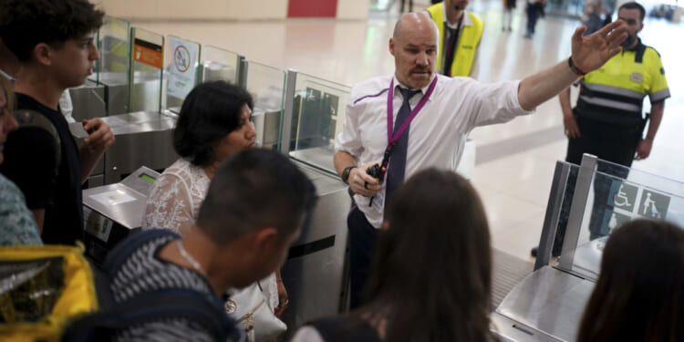 employees giving directions to passengers crowded at the entrance to the platforms at Sants train station in Barcelona