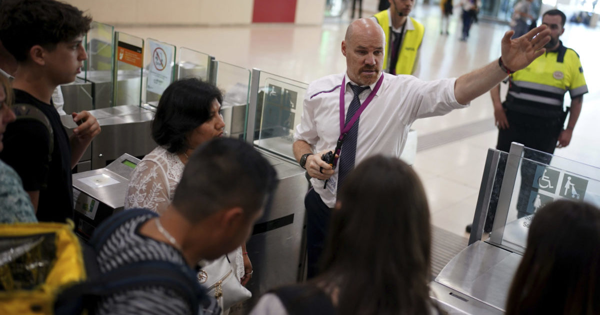 employees giving directions to passengers crowded at the entrance to the platforms at Sants train station in Barcelona