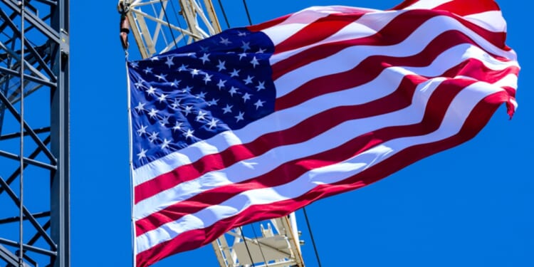 The American flag waves proudly from construction cranes under a brilliant blue sky.