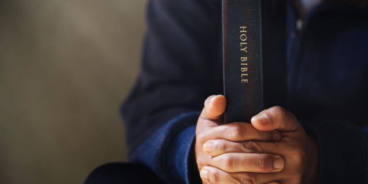 This photo shows hands holding tightly to the Holy Bible.