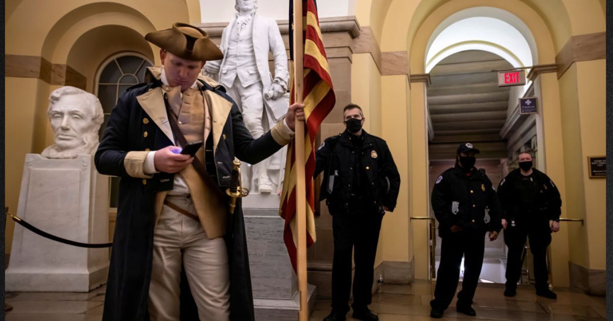 Capitol Police look on as a protester dressed as George Washington checks his phone before being pushed out of the building on Jan. 6, 2021. Supporters of then-President Donald Trump staged a mostly peaceful protest at the Capitol as Congress debated the 2020 presidential election electoral vote certification.