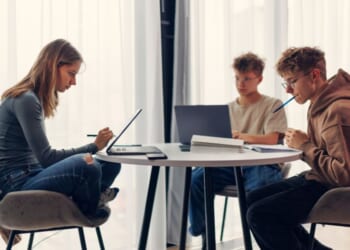 Three teenagers using laptops and smartphones while doing homework.