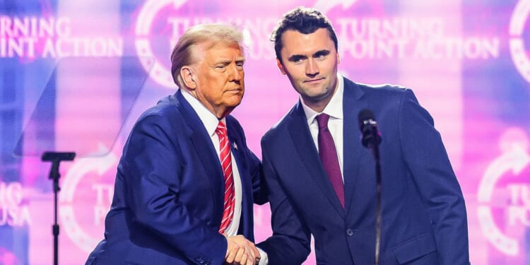 This photo taken on Dec. 22, 2024, shows conservative activist Charlie Kirk shaking hands with President Donald Trump as he speaks on stage at America Fest 2024 in Phoenix, Arizona.