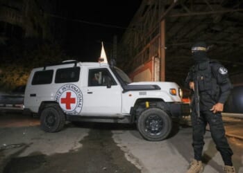 A gunman wearing the uniform of the al-Qassam Brigades, the military wing of Hamas, stands guard as Red Cross vehicles enter a warehouse allegedly to collect coffins containing the bodies of four deceased hostages in Gaza City on Tuesday.